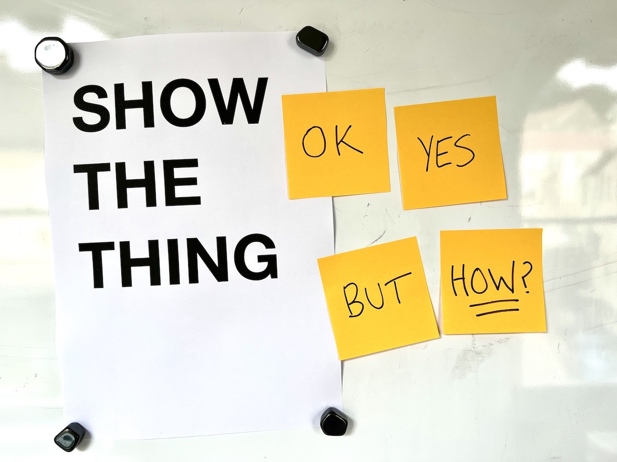 Photo of a poster saying SHOW THE THING and stickies attached saying OK YES BUT HOW?